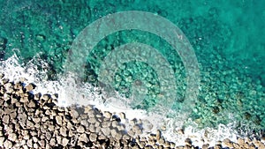 Turquoise transparent water splashing over rocks in ocean. Aerial top view of foamy crystal clear waves of Mediterranean