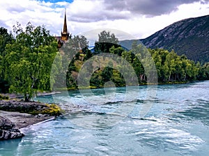 Turquoise water of the Bovra river in Norway with the Lom stave church in the background