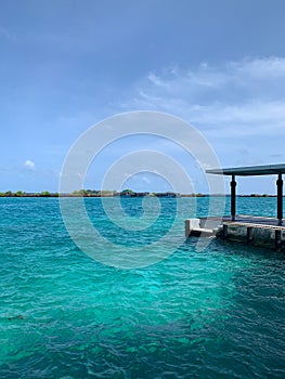 A turquoise water jetty in the Maldives overlooking an island with docked ships