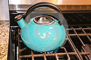 Turquoise water kettle on lit gas stove - textured handle and steel grills and marble countertop - Close-up and selective focus