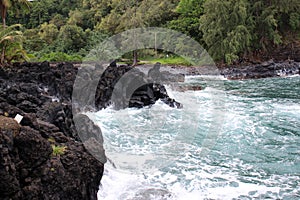 Turquoise water rushing into a black lava rocky cove at Wailua Lookout in Haiku, Maui, Hawaii