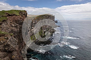 Turquoise water with strong waves on steep cliffs covered in greenery.