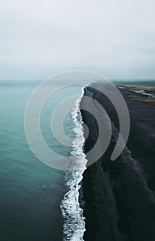 Turquoise water, white foam, and black sand. Magical and calm atmosophere in Vik