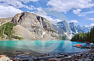 Turquoise waters of beautiful Moraine lake. Snow-covered Rocky mountains in summer day. Canoes on a jetty.