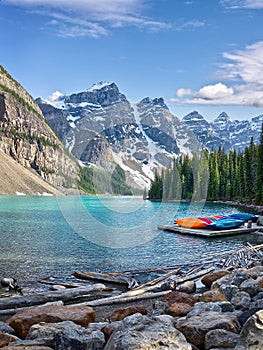 Turquoise waters of beautiful Moraine lake. Snow-covered Rocky mountains in summer day. Canoes on a jetty.