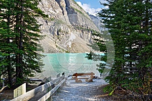 Turquoise waters of beautiful Moraine lake. Snow-covered Rocky mountains in summer day. log bench on the lake.