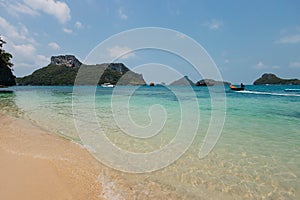 Turquoise waters meet a sandy beach with boats and green hills in the background on a sunny day