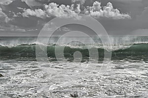 A Turquoise wave breaking on a beach in sea with silver clouds