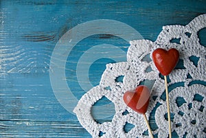 Turquoise wooden background in country style with two red hearts on crocheted lace doily