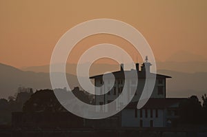 A Tuscan farmhouse and outhouse at sunset, surrounded by hills