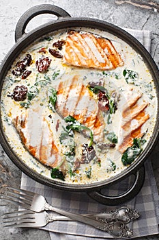 Tuscan pan seared salmon in a delicious creamy sauce with spinach, sun dried tomatoes and parmesan closeup in the pan. Vertical