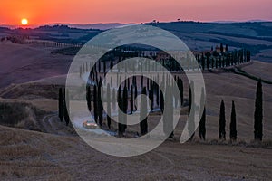 Tuscany, Crete Senesi rural sunset landscape. Countryside farm, cypresses trees, green field, sun light and cloud. Italy