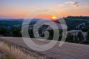 Tuscany, Crete Senesi rural sunset landscape. Countryside farm, cypresses trees, green field, sun light and cloud. Italy