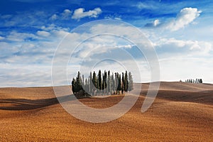 Tuscany, Italy - scenic view of tuscan landscape with rolling hills, small cypress trees forest and blue sky with clouds