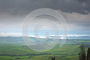 Tuscany, rural landscape. Countryside farm, cypresses trees, green field, cloudy day