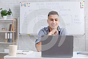 Tutor evaluates students knowledge. Young man looking at laptop in classroom