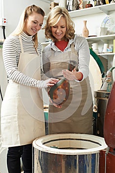 Tutor With Female Student In Pottery Studio Firing Vase In Kiln