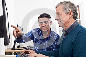 Tutor Helping Mature Man In Computer Class