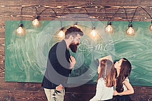 Tutor teach children students in classroom. Teacher write with chalk on chalkboard. Little girls listen to bearded man