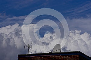 TV antenna, satellite dish on blue cloudy sky background.