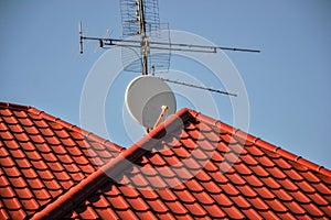 TV antennas and satellite dish for television mounted on the tiled roof of house isolated on blue sky background in countryside