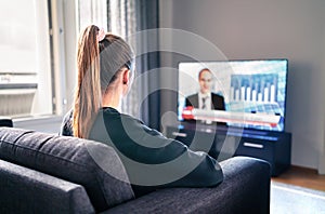 Tv news. Woman watching television broadcast in home living room. Reporter, anchor and studio host in screen with newscast.