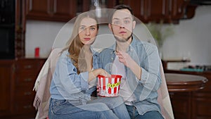 TV POV of absorbed millennial couple watching movie eating popcorn. Portrait of engrossed Caucasian young man and woman
