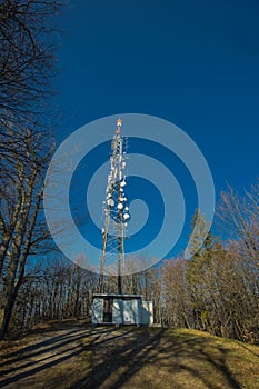 Tv or radio antenna, communications tower on the top of the hill on a small clearing and blue skies. Antenna above Lasko at Malic