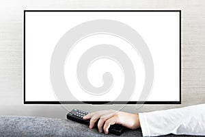 TV remote control in male hand in front of widescreen TV set with blank screen on white wall background. Young guy switches