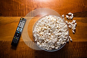 Tv remote control and popcorn on a wooden brown coffee table