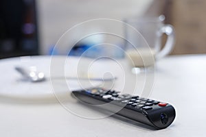 TV remote control on table, in kitchen next empty plate and cup, end breakfast