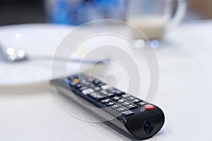 TV remote control on table, in kitchen next empty plate and cup, end breakfast