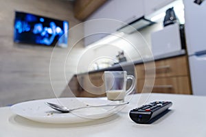 TV remote control on table, in kitchen next empty plate and cup, end breakfast