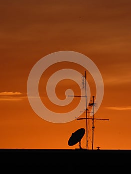 TV satellite dish and antennas on a house roof at sunset