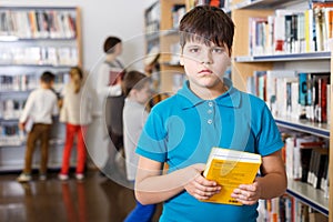 Tween boy with book in school library