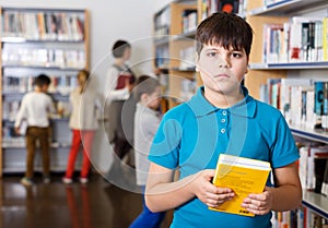 Tween boy with book in school library
