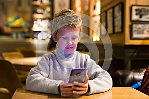 Tween boy carried away with phone at table in cafe