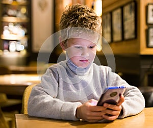 Tween boy carried away with phone at table in cafe