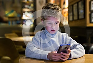 Tween boy carried away with phone at table in cafe