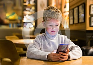 Tween boy carried away with phone at table in cafe