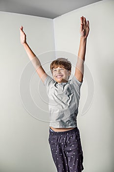 A tween boy jumping up in the air in excitement against a white corner wall