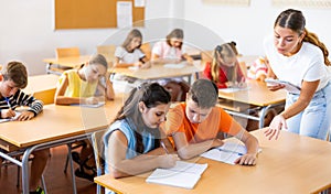 Tween boy peeking at workbook of girl classmate at lesson