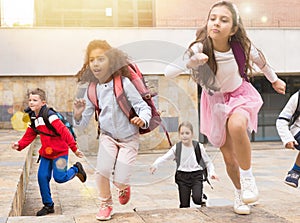 Tween boys and girls with school backpacks running in schoolyard