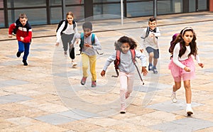 Tween boys and girls with school backpacks running in schoolyard