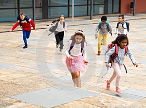 Tween boys and girls with school backpacks running in schoolyard