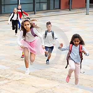 Tween boys and girls with school backpacks running in schoolyard