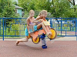 Tween caucasian girls sits on toy wooden motorbike on playground