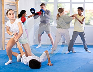 Tween girl applying armlock to face-down boy in mock fight at self-defense classes