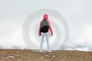 Tween girl with backpack looking on beautiful mountains in clouds, family travel concept