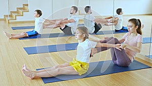 Tween girl with brother sitting on mat in modern yoga studio during family workout, doing exercises in pair